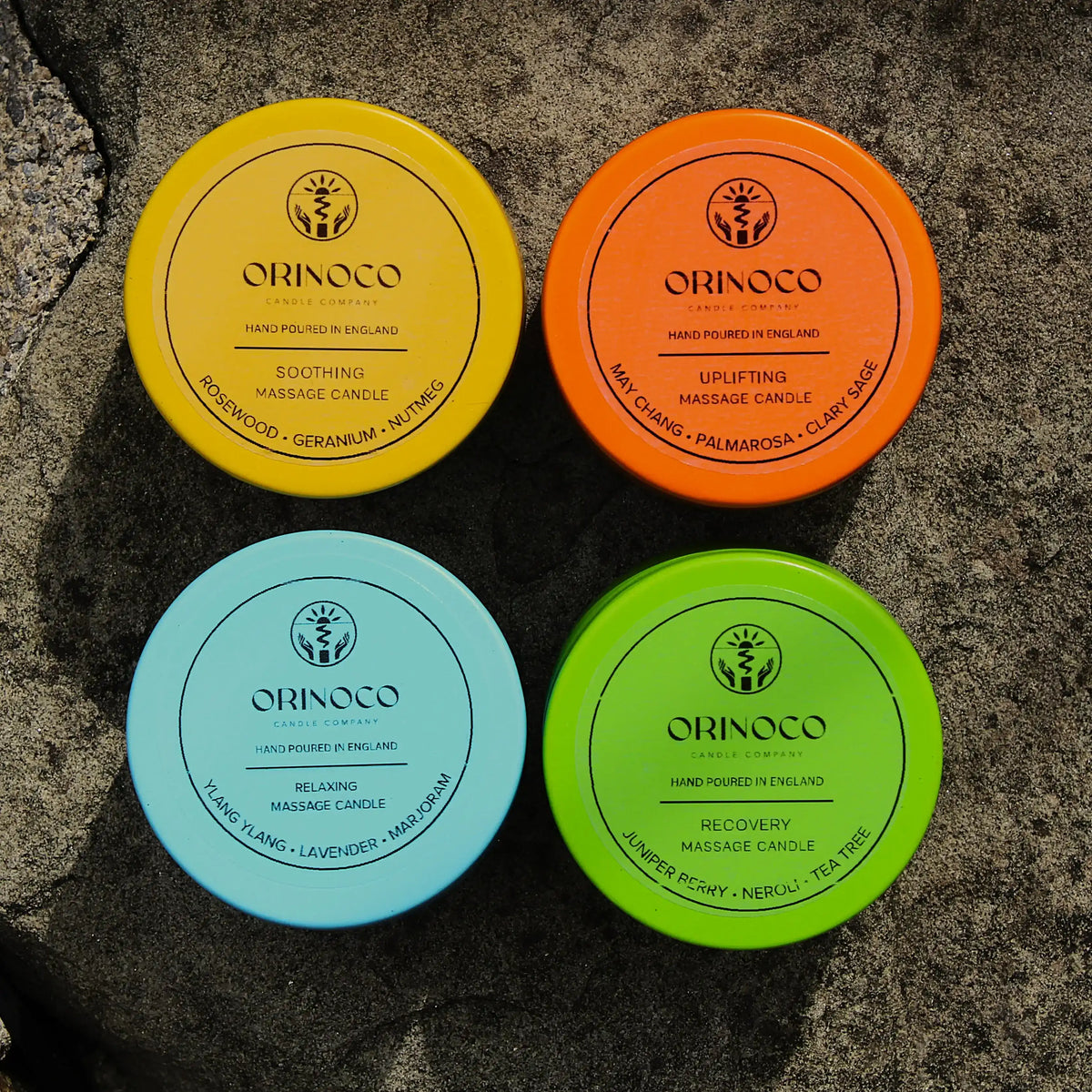 Four colorful Orinoco massage candles in yellow, orange, blue, and green on a stone surface.