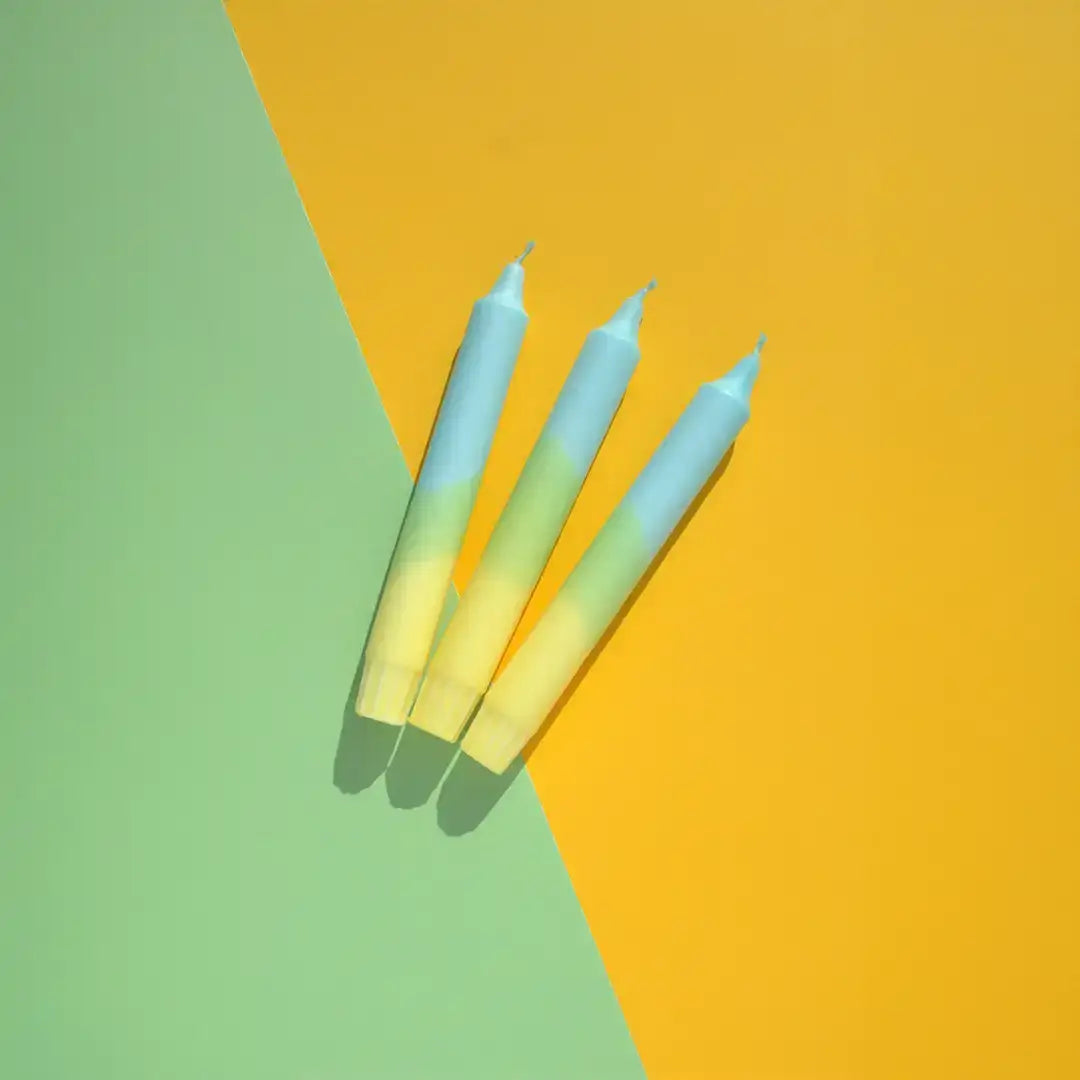 Three blue and yellow gradient taper candles on a green and yellow background.