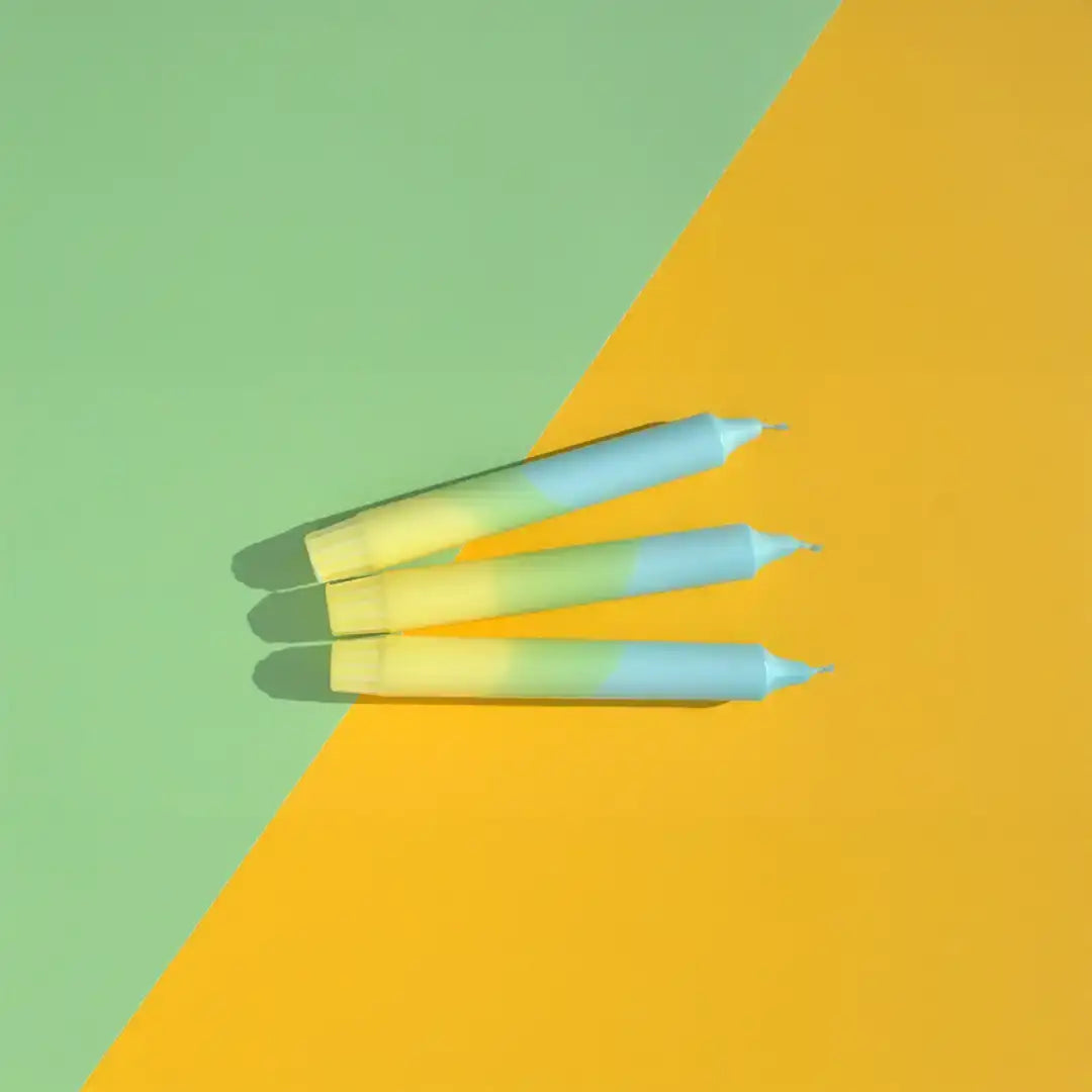 Three pastel blue and yellow skincare sticks on a green and yellow split background.