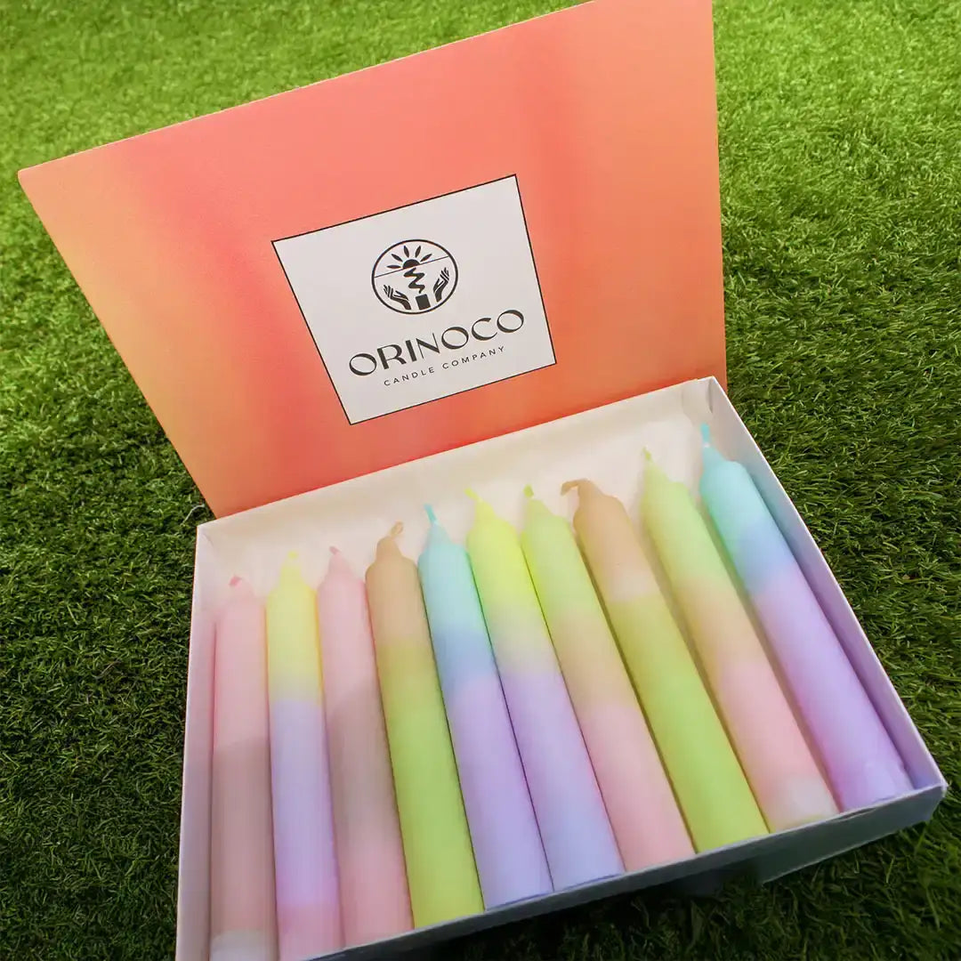 Orinoco Candle Company box of colorful pastel gradient taper candles on green grass.