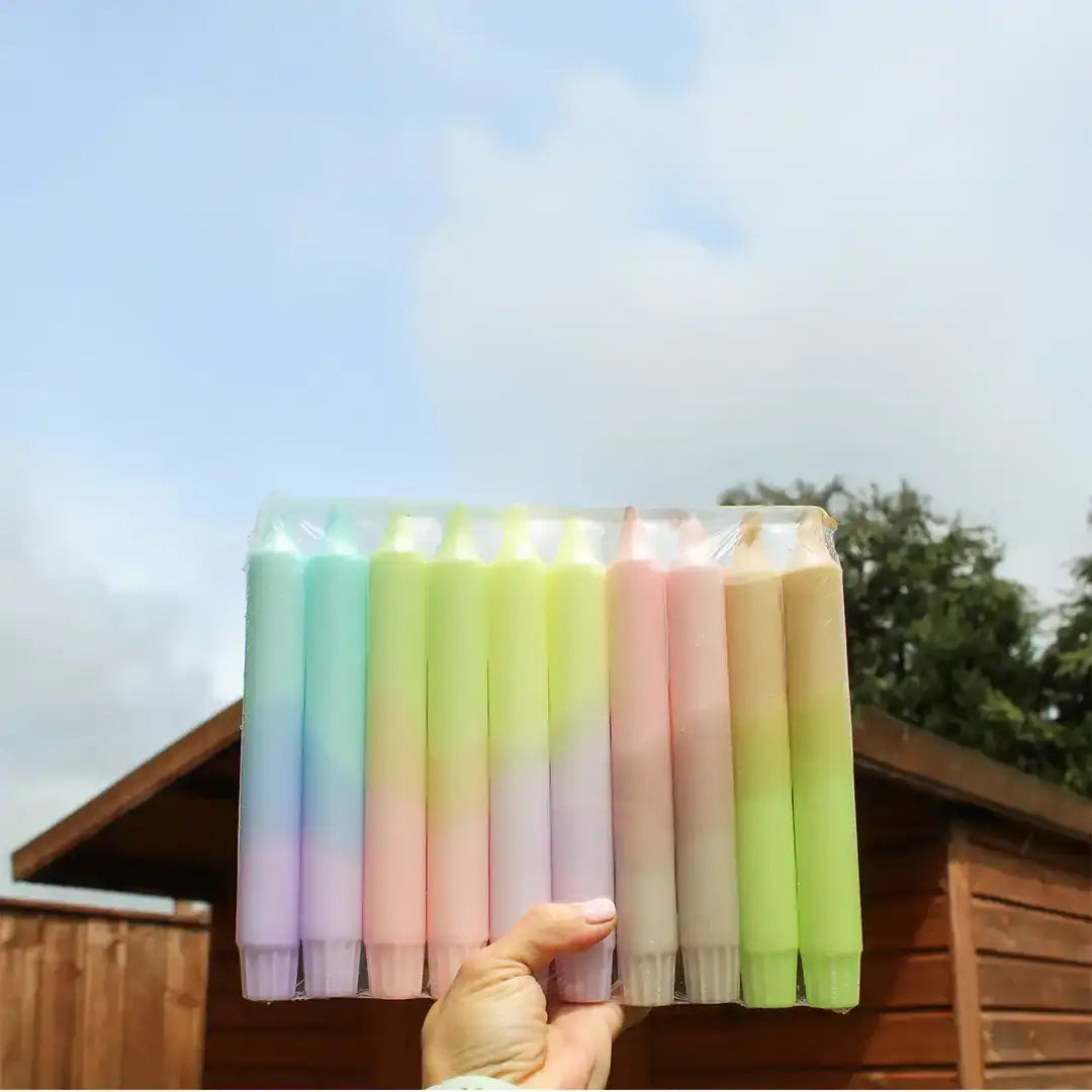 A pack of colorful pastel gradient taper candles held against a blue sky background.