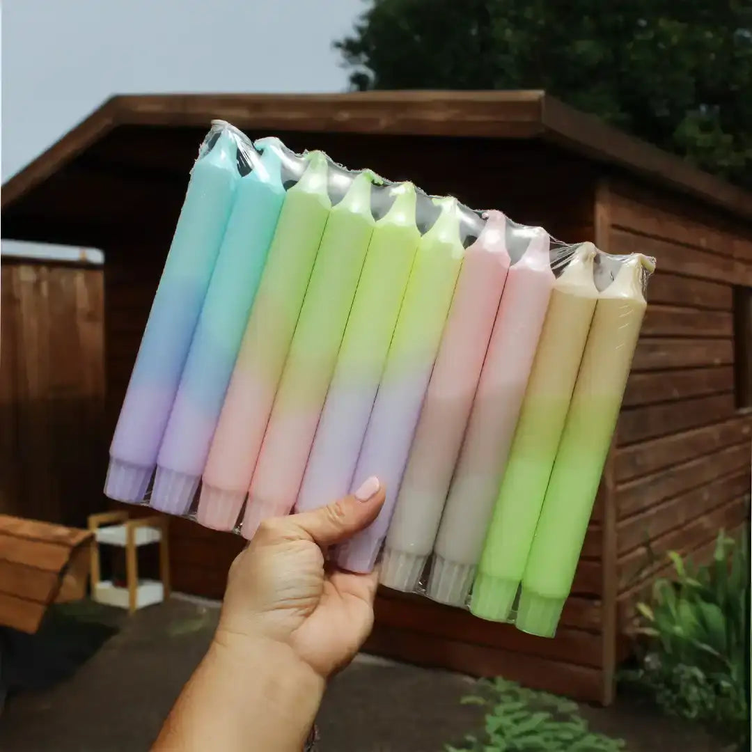 Hand holding a pack of colorful pastel gradient taper candles outdoors.