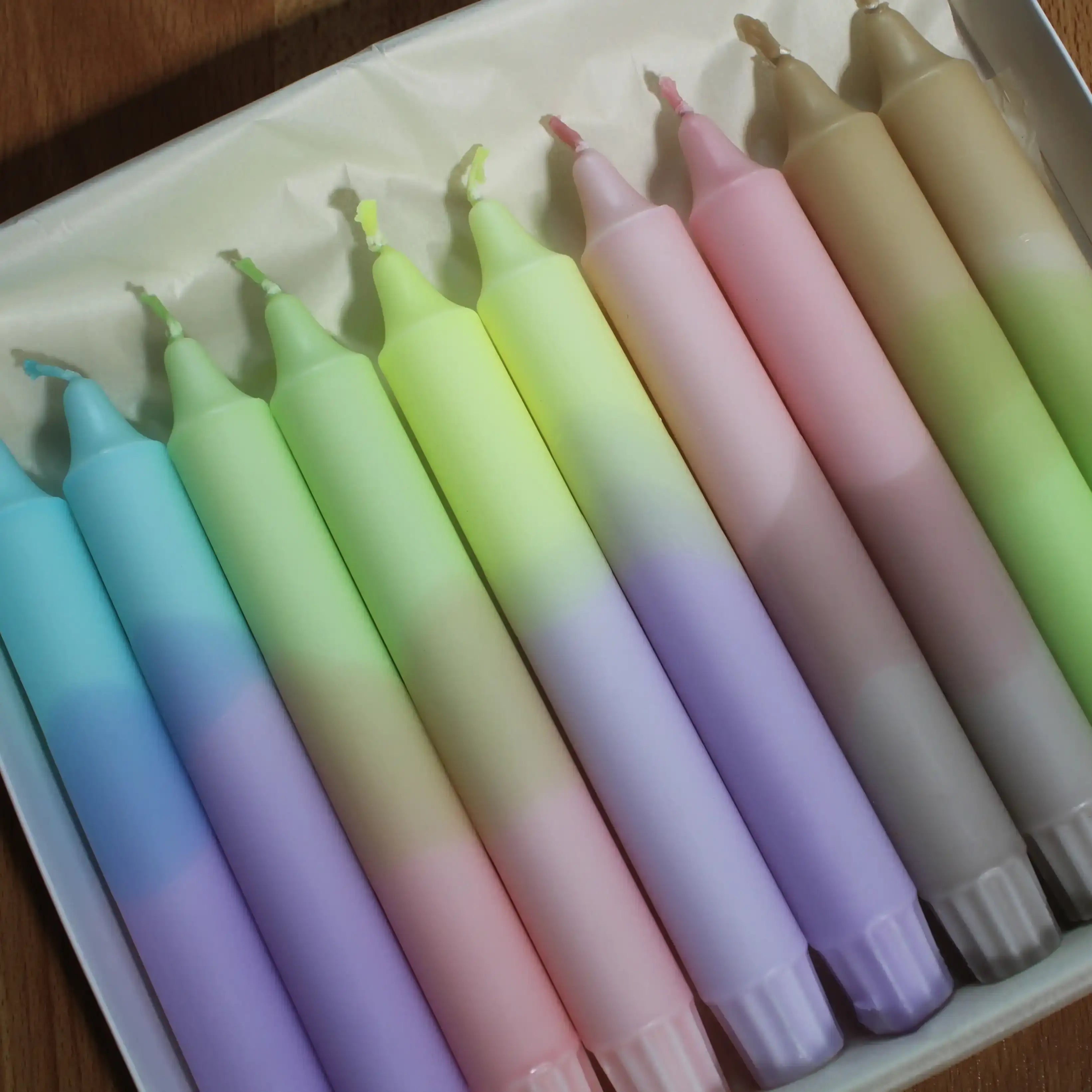 Assorted pastel gradient taper candles in a white tray.