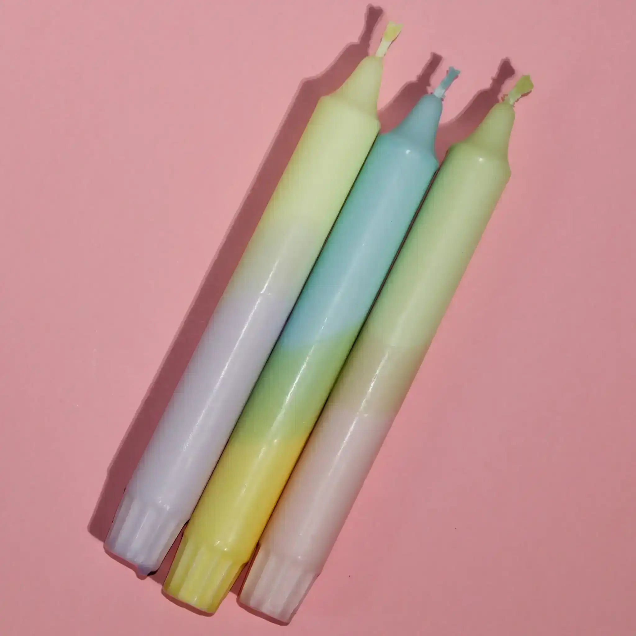 Three pastel-colored gradient taper candles on a pink background