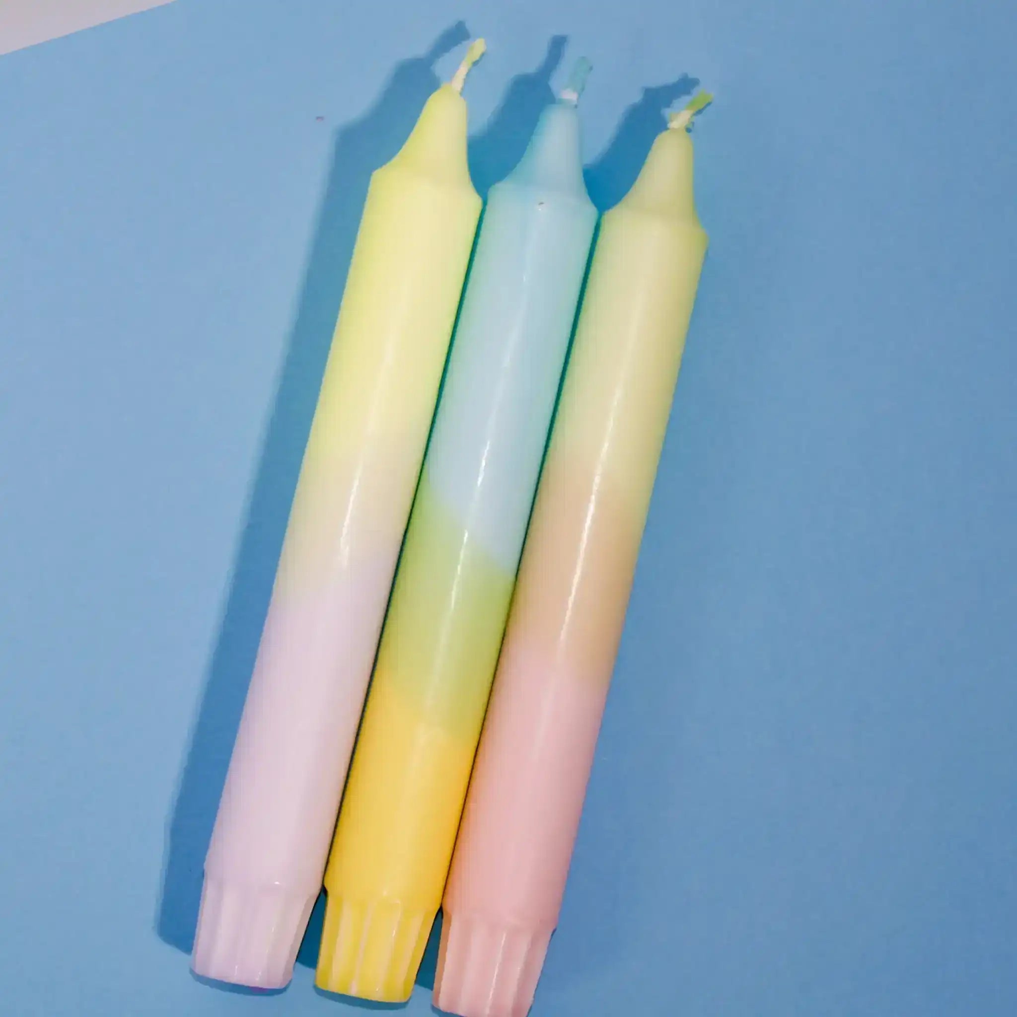 Three pastel gradient taper candles in yellow, blue, and pink against a blue background.