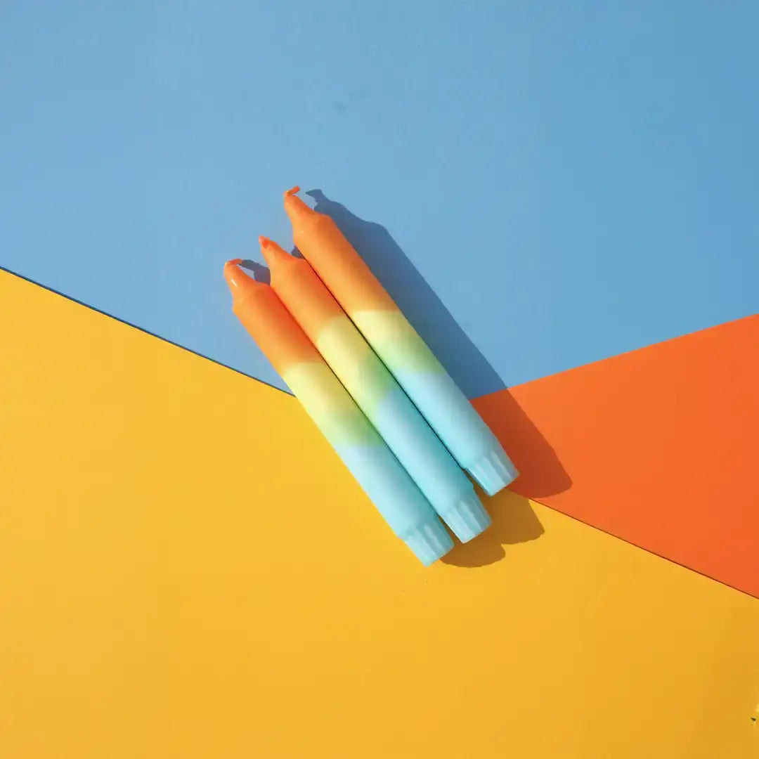 Set of colorful gradient taper candles on a blue, orange, and yellow background.