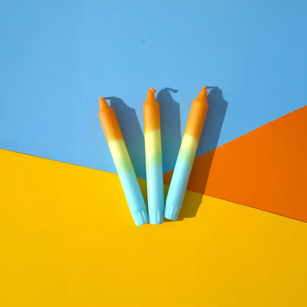Three ombre orange and blue tapered candles on a blue and yellow background.