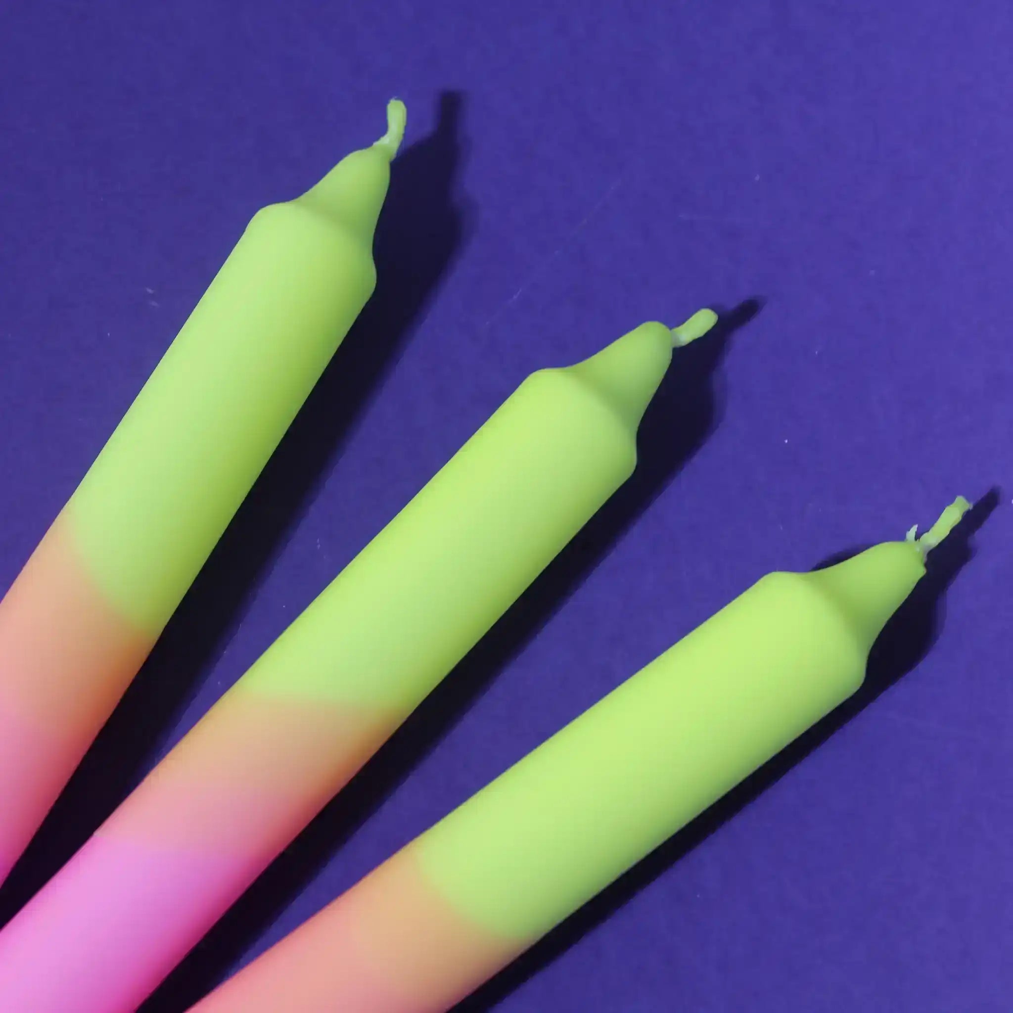 Three neon gradient candles in yellow, green, and pink against a deep purple background.