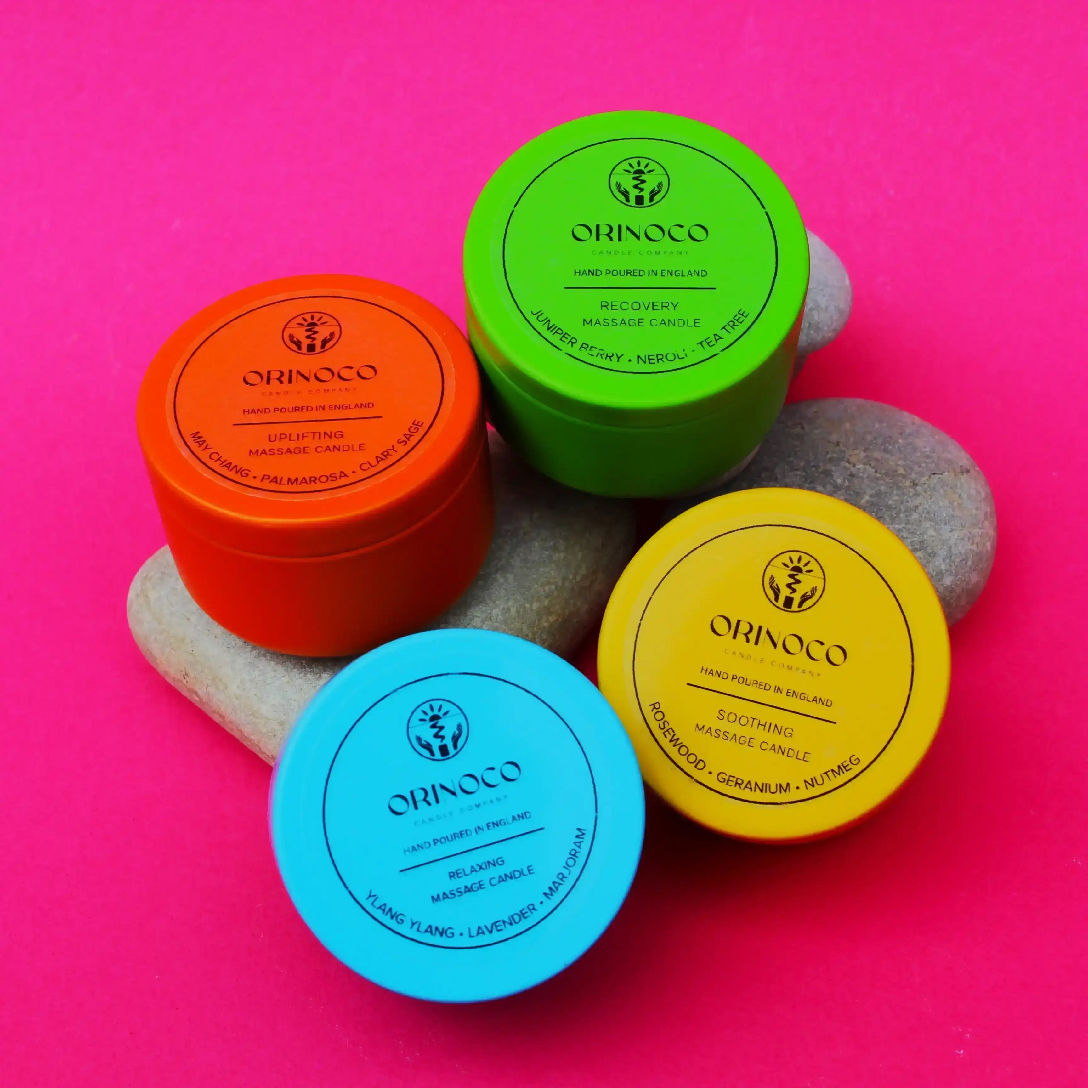 Three colorful Orinoco Skincare massage candles on smooth grey stones against a pink background.
