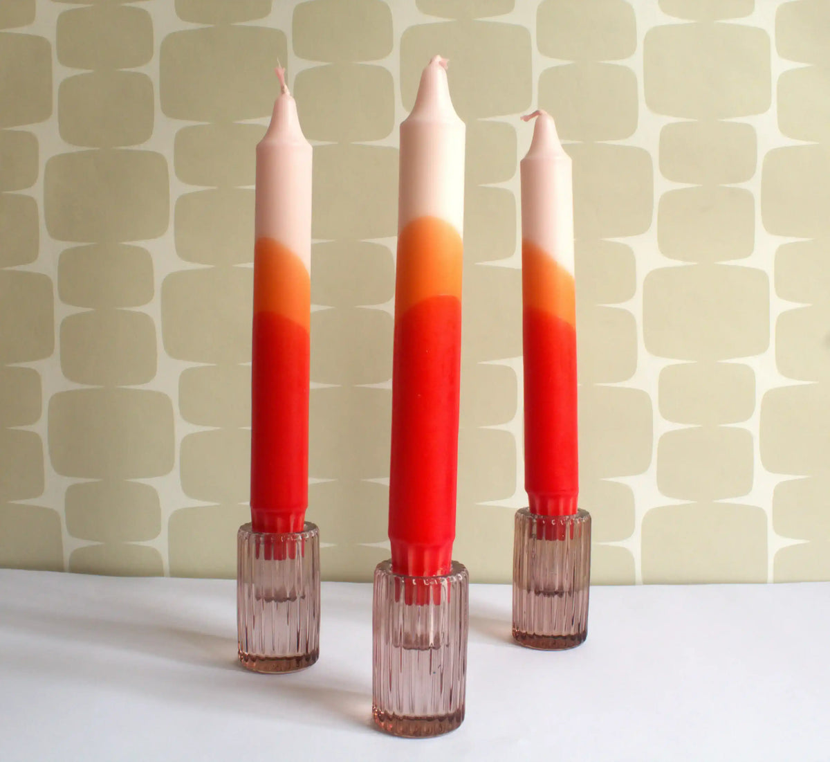 Three gradient ombre candles in red, orange, and peach tones in ribbed glass holders.