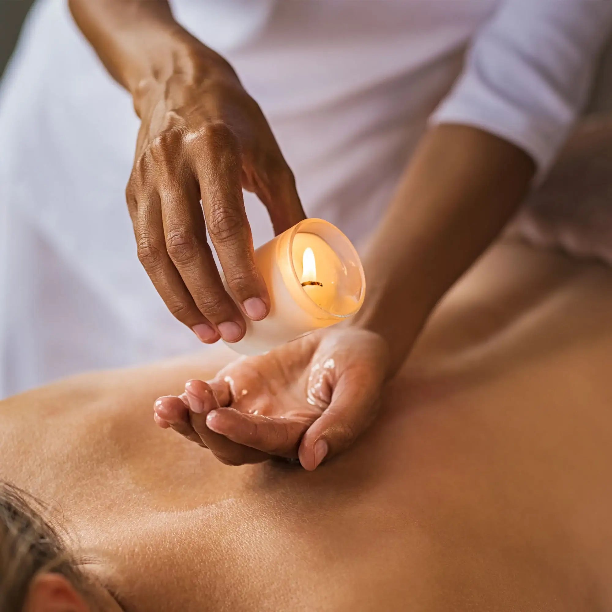 Therapist pouring warm natural massage oil into hand for a relaxing body treatment.
