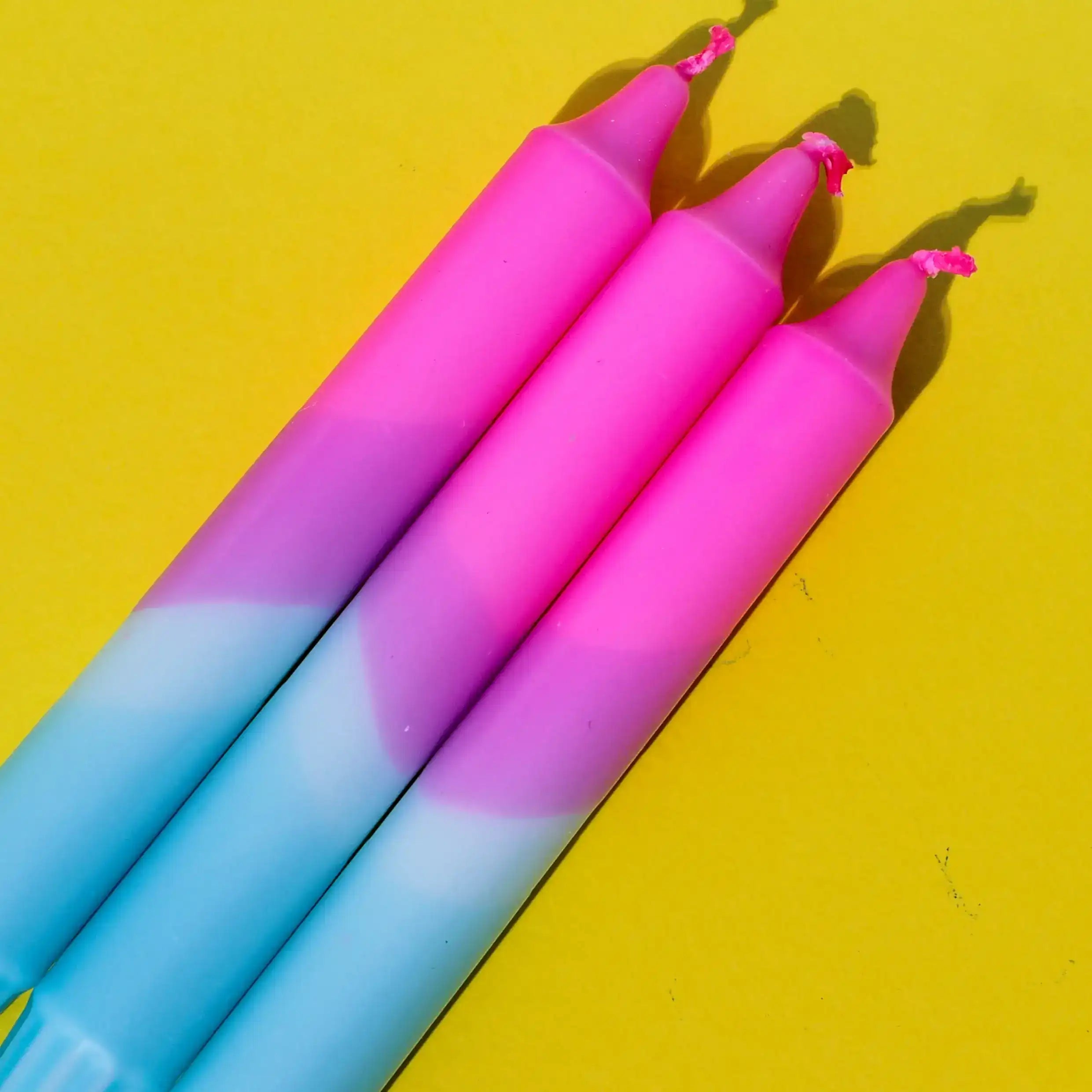 Three pink and blue gradient taper candles on a bright yellow background.