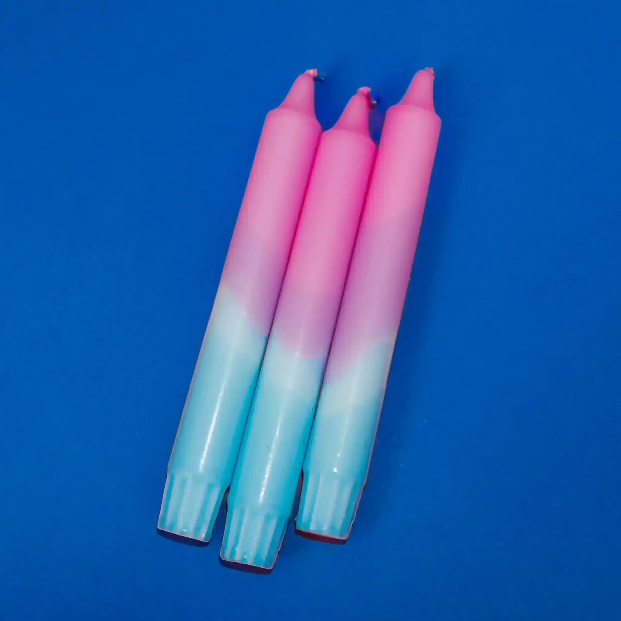 Three pink and blue gradient taper candles against a solid blue background