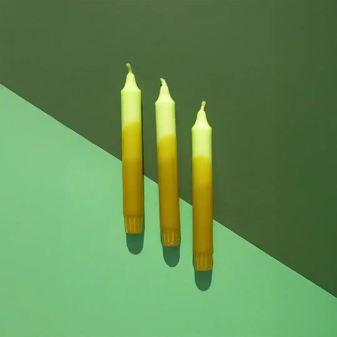 Three yellow gradient taper candles against a two-tone green background.