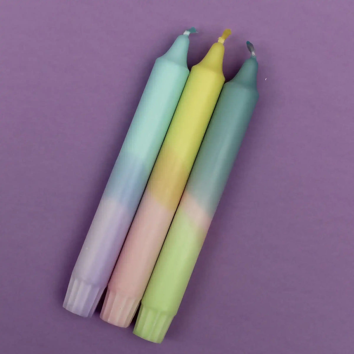 Three pastel-colored gradient taper candles on a purple background.