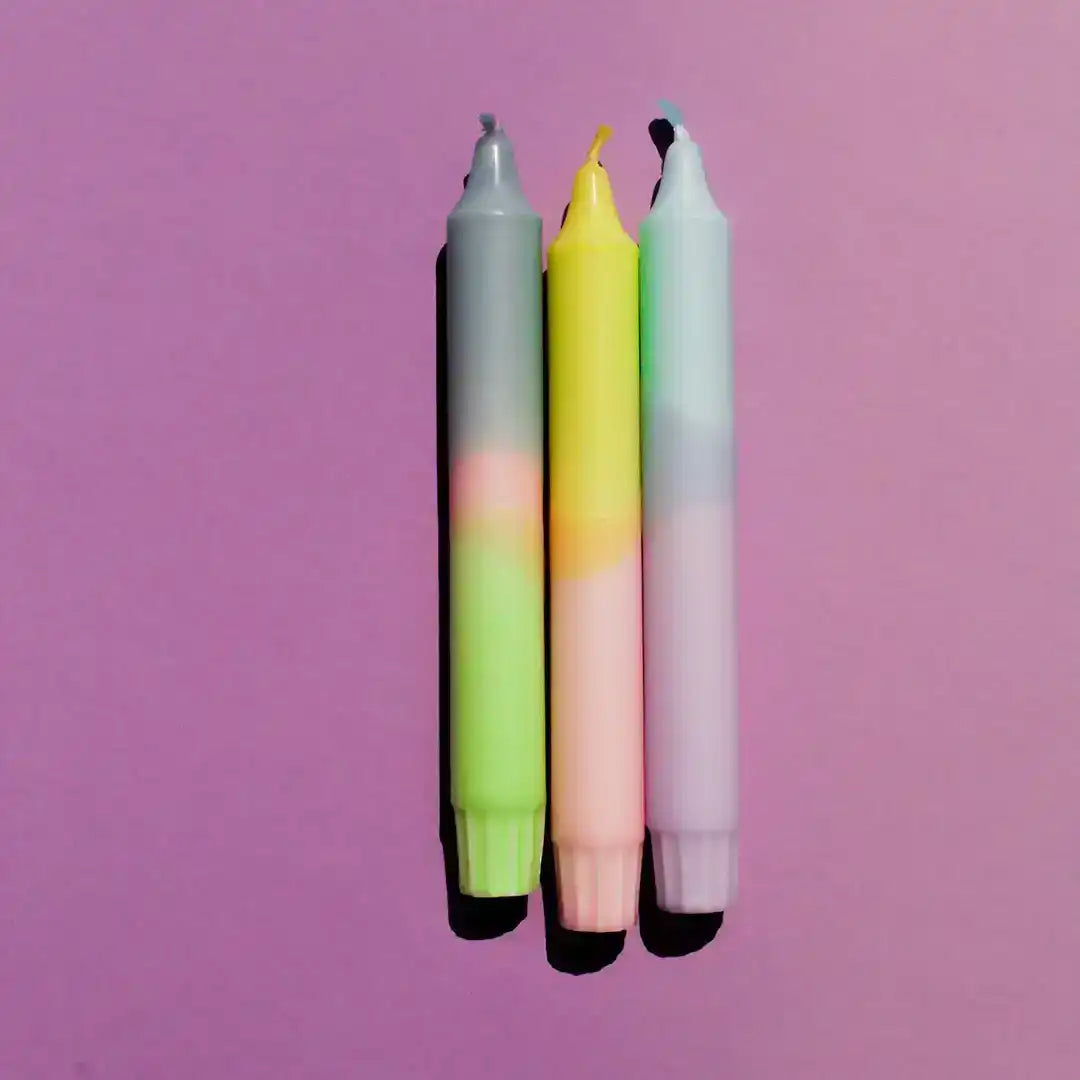 Three colorful pastel gradient candles against a vibrant purple background.
