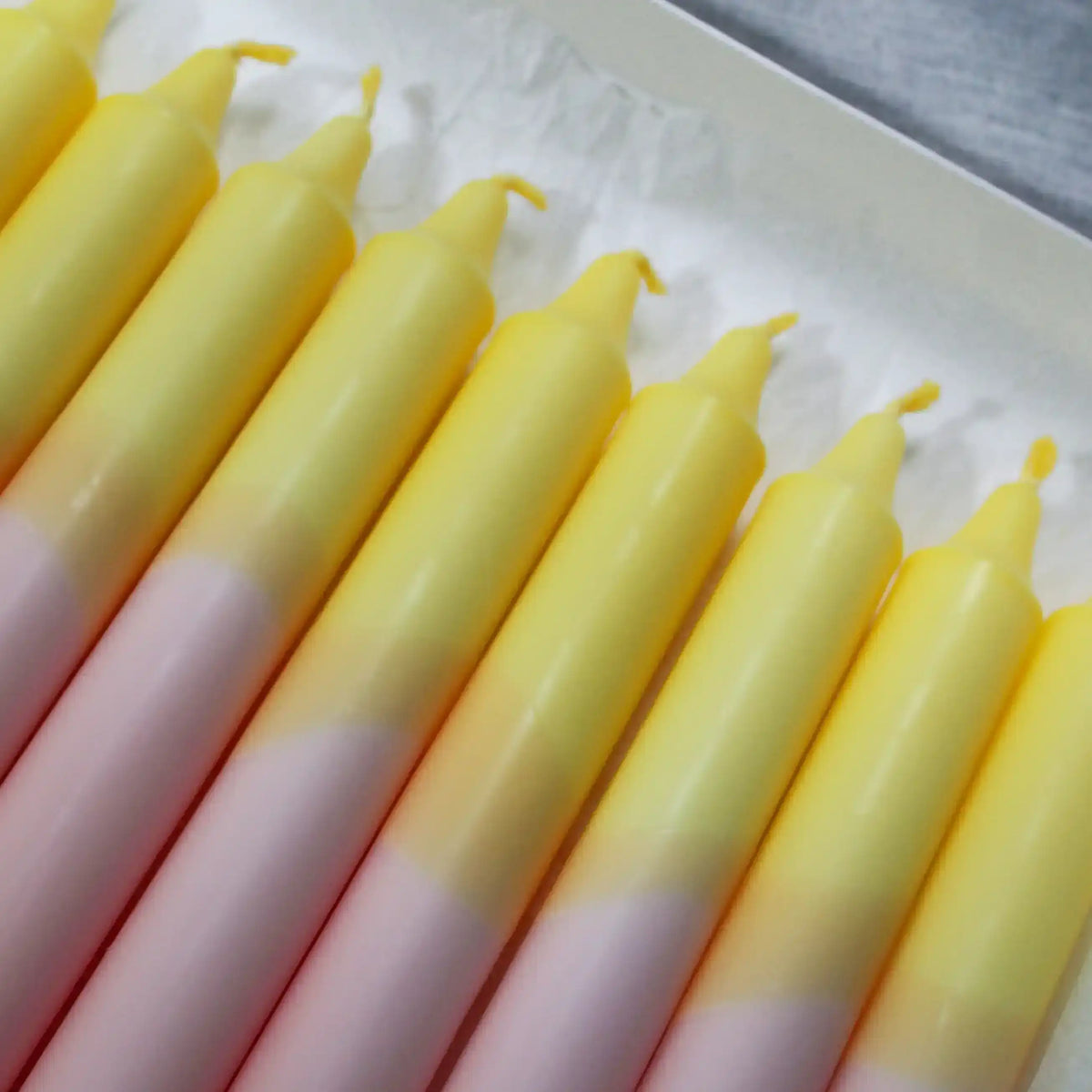 A row of yellow and pink gradient taper candles in a white box.