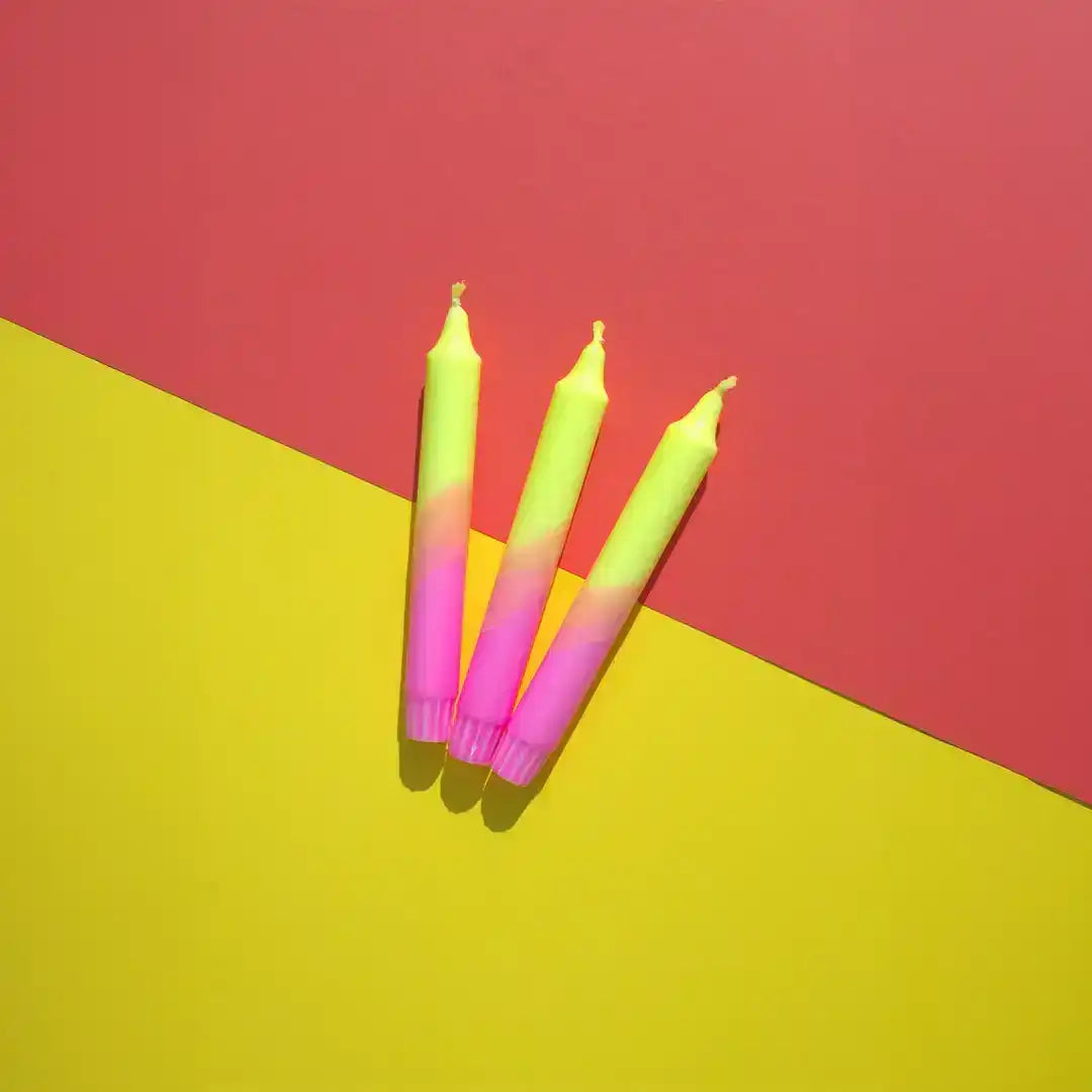 Three yellow and pink gradient taper candles on a split pink and yellow background.