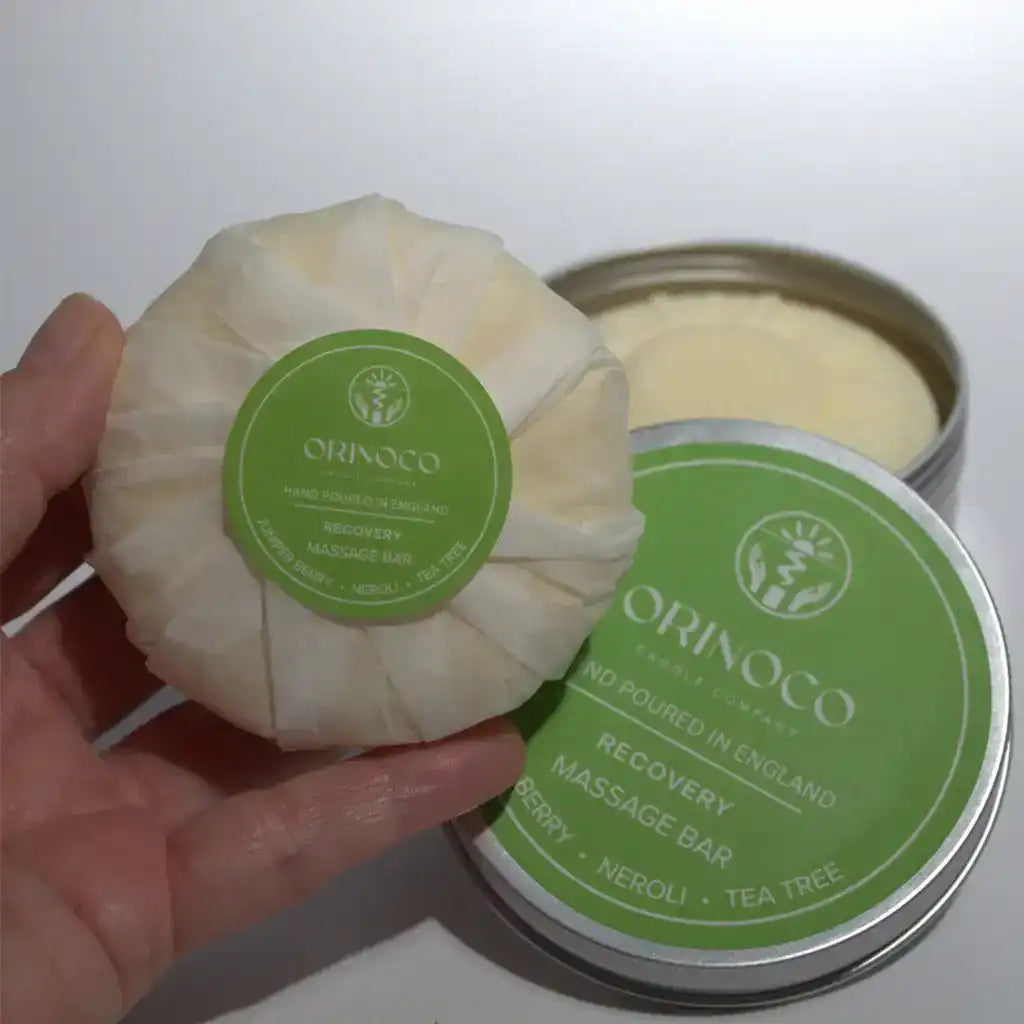 Hand holding an Orinoco Recovery Massage Bar with its matching tin container.