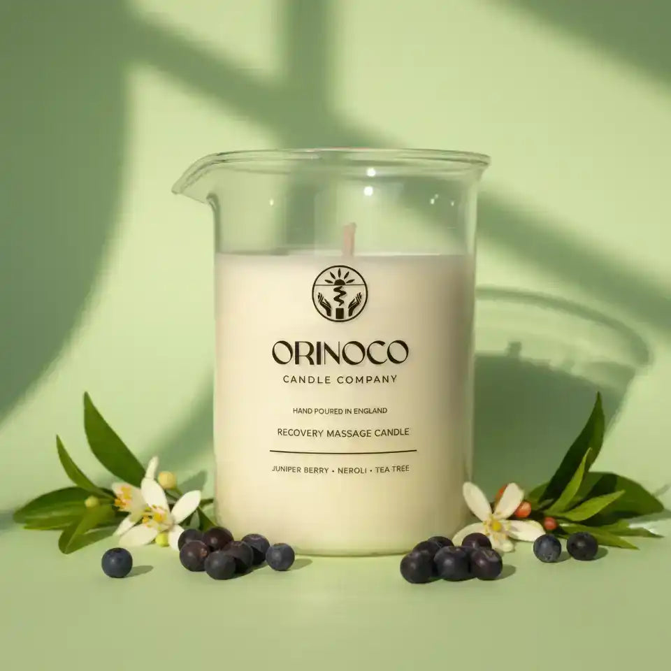 Orinoco Skincare Recovery Massage Candle in a glass jar with blueberries and white flowers.