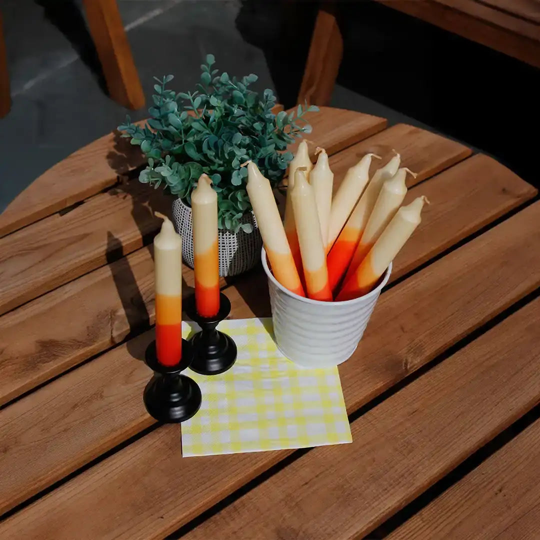 Sunset gradient taper candles in a white ceramic holder on a wooden table with greenery.