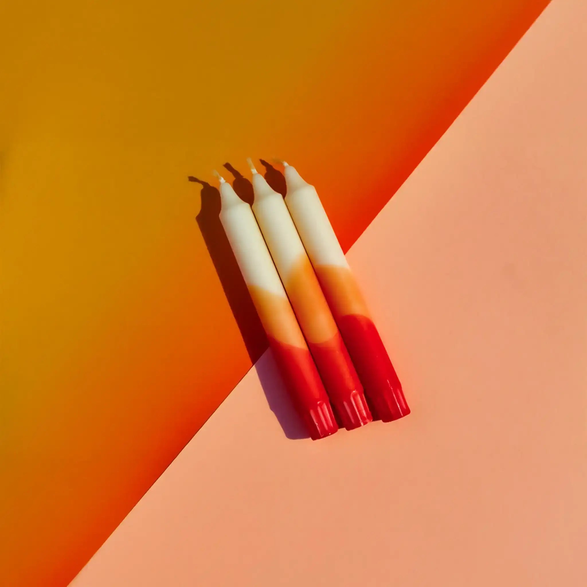 Three gradient sunset-colored taper candles on an orange and peach background.