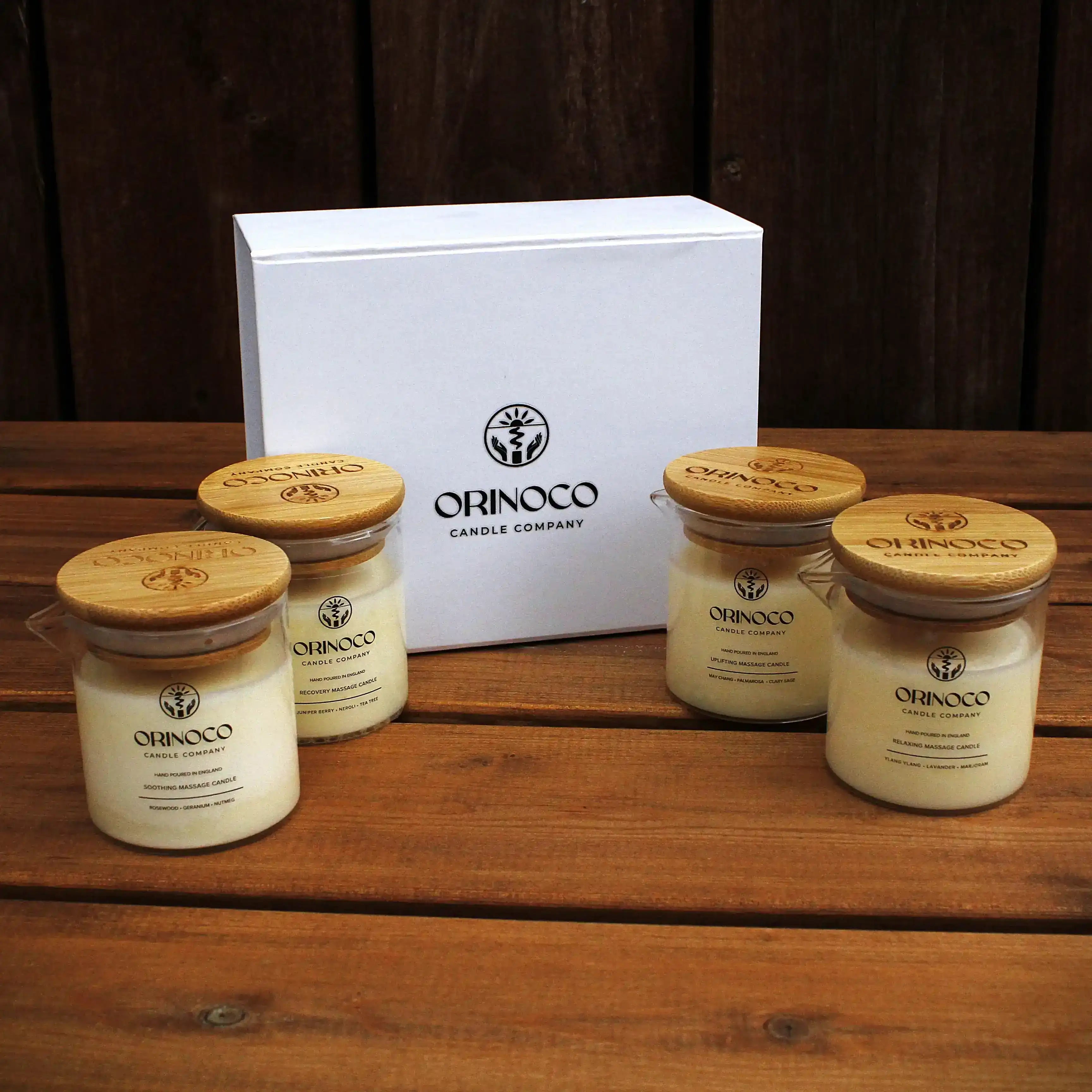 Four Orinoco Candle Company massage candles with wooden lids and a white gift box on a wooden table.