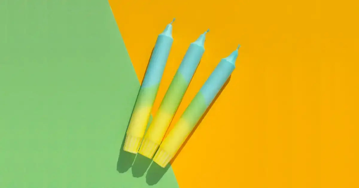 Three gradient blue and yellow tapered candles on a split green and orange background.