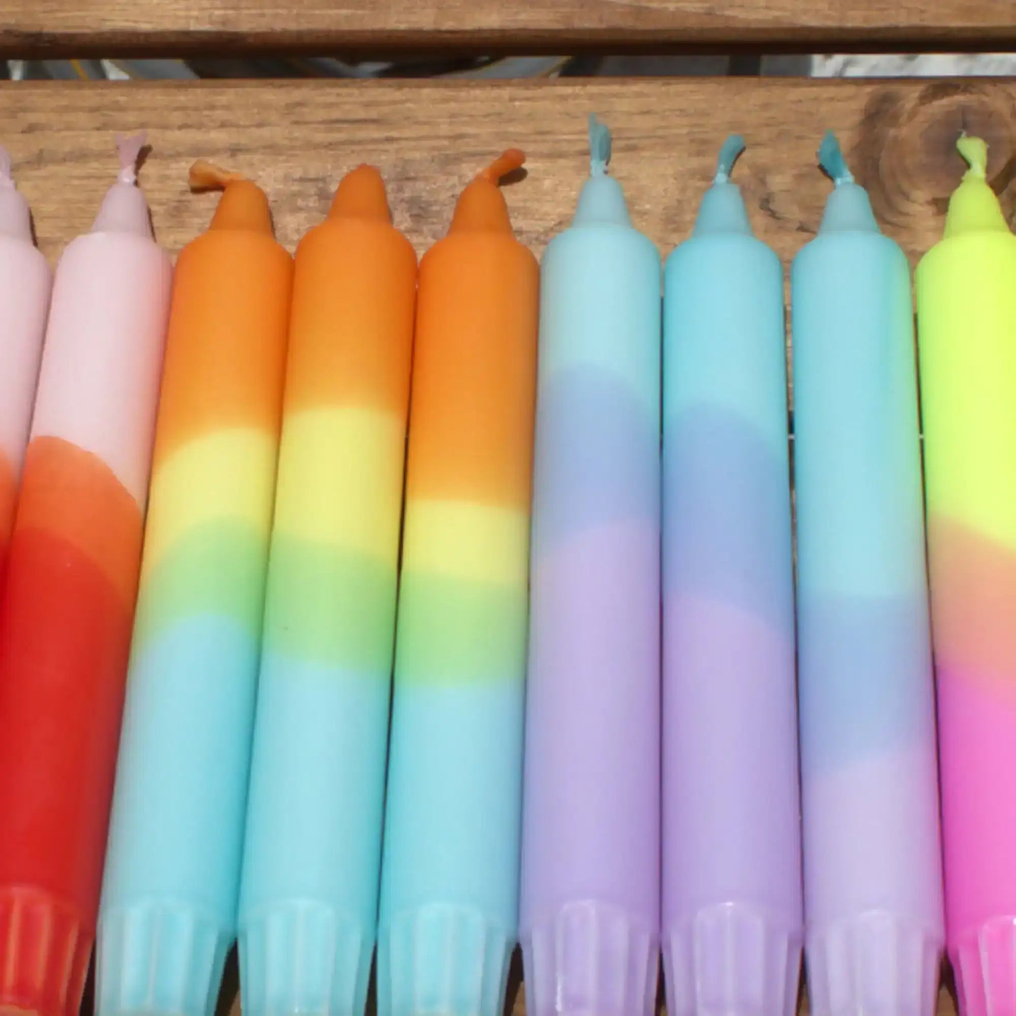Colorful gradient taper candles in pastel rainbow hues arranged on a wooden surface.
