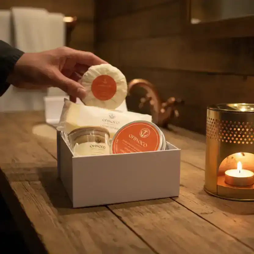 A hand placing a skincare product into a gift box with candles and spa accessories.