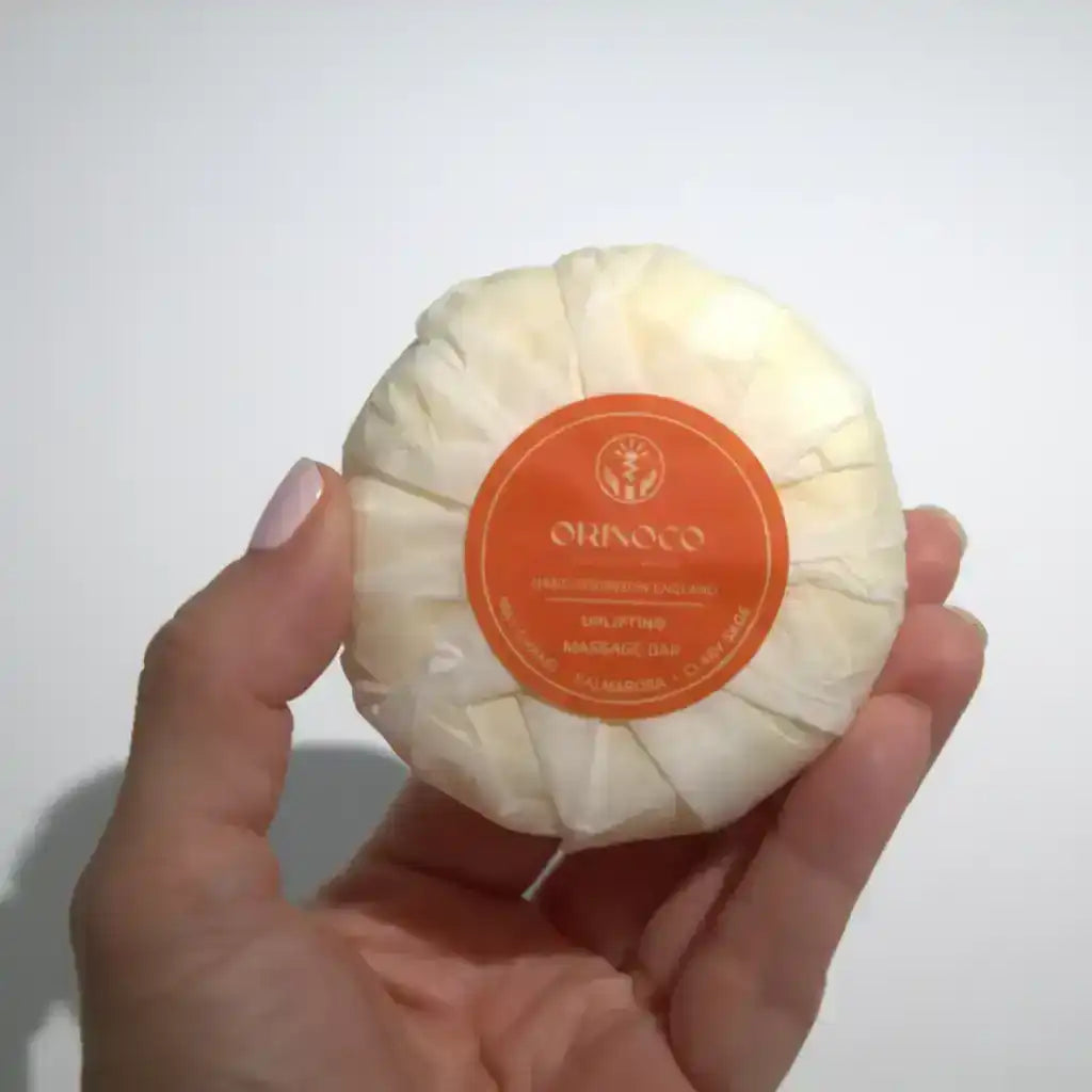 Hand holding an Orinoco Uplifting Massage Bar wrapped in white protective paper.