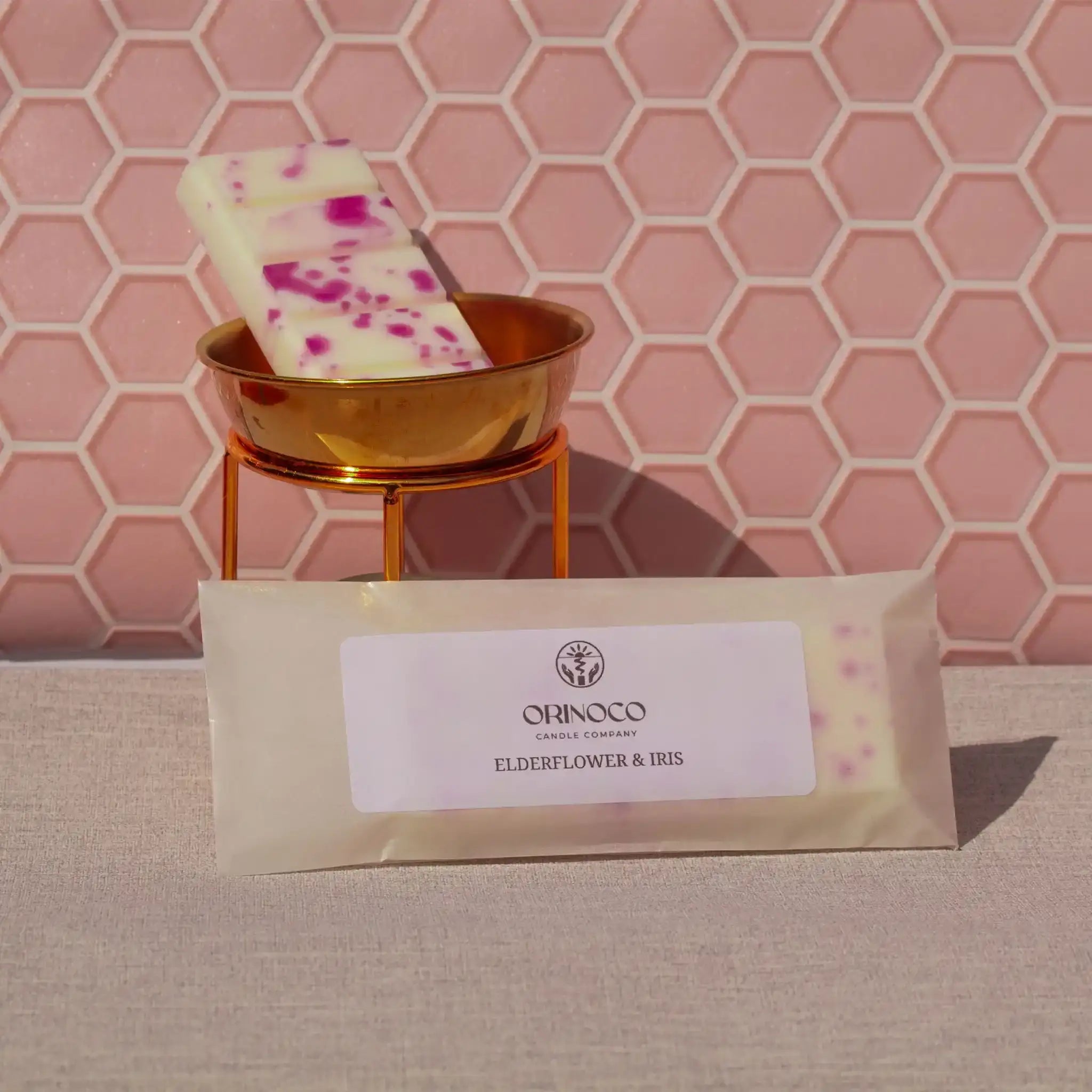 Elderflower & Iris patterned soap bar in a gold dish against a pink hexagonal tile background.