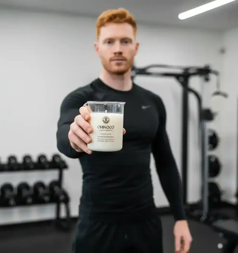 A man in a gym holding a white Orinoco candle in a glass jar.