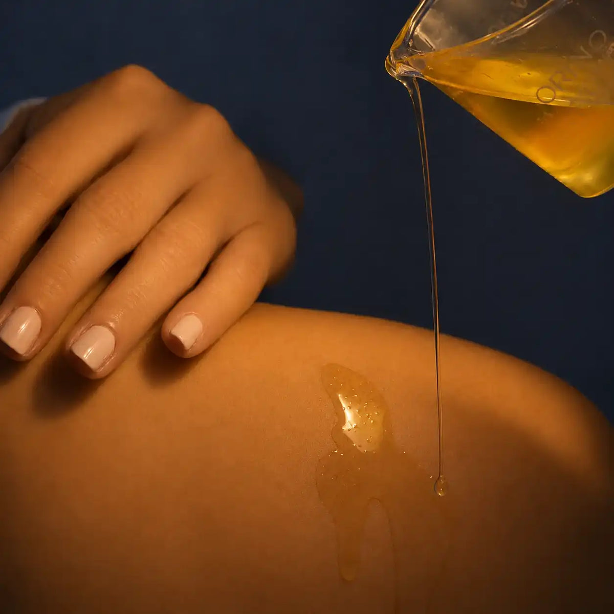 Golden body oil being poured onto a woman's skin for a hydrating spa treatment.