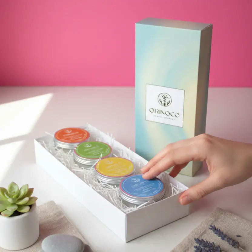 Hand reaching for a blue Orinoco skincare tin in a gift set box with colorful natural balms.