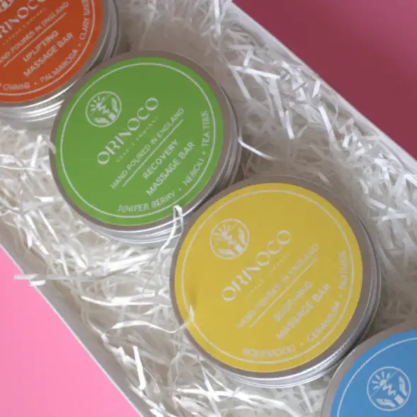 Assorted Orinoco natural massage bars in colorful tins nestled in white shredded paper.