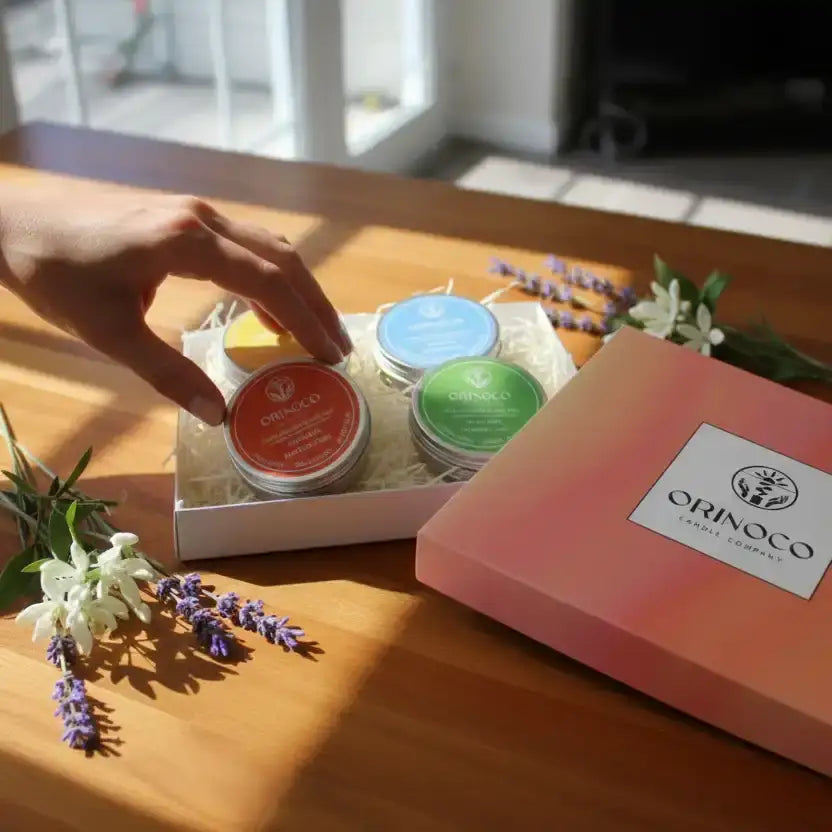 Hand reaching for Orinoco Candle Company tins in a gift box with lavender flowers.